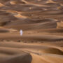 A local man dressed in a traditional white thobe walks across the dunes of the Wahiba Sands desert in Oman.