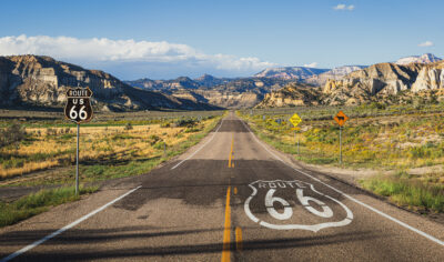 Scenic panoramic view of long straight road on famous Route 66 with historical street signs and paintings in classic american wild western mountain scenery in beautiful golden evening light at sunset